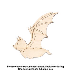 May include: A wooden bat cutout with outstretched wings, featuring detailed etched lines. The bat is light brown and appears to be flying. The image includes text at the bottom: "Please check exact measurements before ordering. See listing images & listing info."