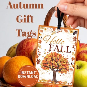 May include: A rectangular gift tag with a black ribbon loop featuring the text Hello FALL in brown script and block letters. The design includes a central tree with orange and yellow leaves, surrounded by a border of autumn foliage and flowers.
