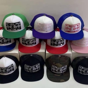 Puede incluir: Una colección de gorras de camionero en varios colores, incluyendo verde, morado, azul, rojo y negro. Cada gorra presenta un panel frontal blanco con un parche rectangular que muestra un logotipo y texto. Las gorras tienen la parte trasera de malla y viseras curvas.