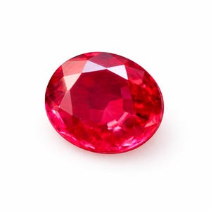 Könnte beinhalten: Ein facettierter, oval geformter Rubin-Edelstein. Der Edelstein hat eine leuchtend rote Farbe mit mehreren Facetten, die das Licht reflektieren. Der Rubin ist vor einem weißen Hintergrund platziert, der seine Farbe und Klarheit hervorhebt. Dieser Edelstein ist für Schmuck geeignet.