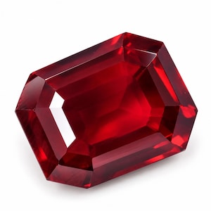 May include: A vibrant, deep red gemstone cut into a rectangular shape with bevelled edges. The stone features a faceted surface that reflects light, creating bright highlights and dark, saturated crimson tones throughout its transparent body.