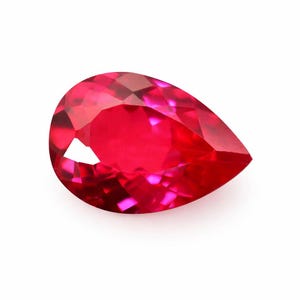 May include: A faceted, pear-shaped ruby gemstone. The gem is a vibrant, deep red colour, with multiple facets catching the light. The gemstone is set against a white background.