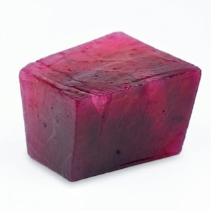 Puede incluir: Un bloque rectangular de jabón translúcido con un patrón jaspeado de color magenta intenso y morado oscuro. La superficie del jabón tiene una textura suave y ligeramente irregular con variaciones internas visibles en la densidad del color.
