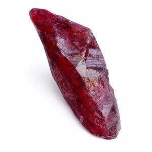 May include: A raw, uncut ruby gemstone, displaying a rich, deep red colour. The ruby exhibits a crystalline structure with visible facets and a slightly rough texture. The gemstone is set against a white backdrop, accentuating its natural form and colour.