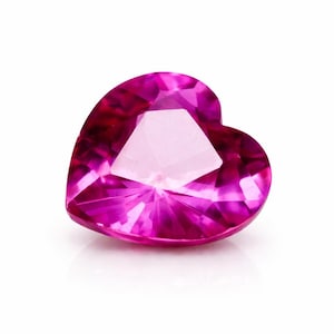 May include: A heart-shaped, faceted gemstone in a vibrant shade of pink. The gem's multiple facets reflect light, creating a sparkling effect. The gemstone is set against a white background, highlighting its colour and shape.