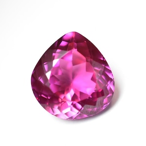 May include: A faceted, pear-shaped gemstone in a vibrant shade of pink. The gem's multiple facets reflect light, creating a sparkling effect. The gemstone is set against a white background.
