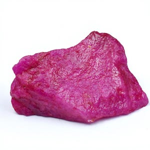 Puede incluir: Una gema de rubí en bruto, de color rojo rosado intenso. La superficie de la piedra tiene una apariencia texturizada, con bordes irregulares y un aspecto natural sin pulir. La gema se encuentra sobre un fondo blanco.