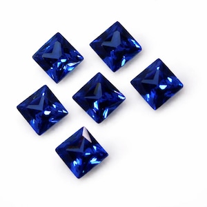 Puede incluir: Seis gemas facetadas de corte cuadrado en un tono azul profundo y vibrante. Las gemas están dispuestas sobre un fondo blanco, mostrando su claridad y brillo. Cada piedra tiene una forma geométrica simétrica.