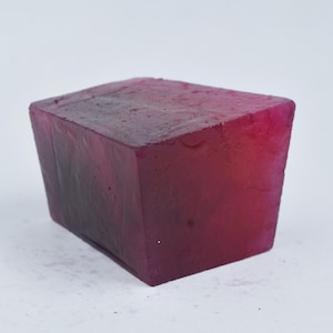May include: A rectangular block with a translucent, deep red appearance. The edges are slightly uneven, and the surface has a subtle texture. The colour transitions from a darker shade at the base to a brighter red towards the top.
