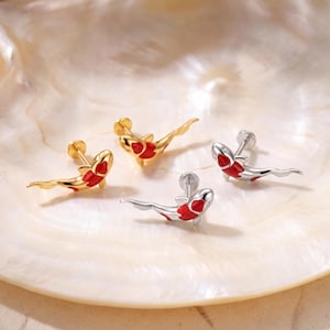 May include: Four stud earrings shaped like koi fish, featuring two gold-toned and two silver-toned pieces. Each earring has a flat back post and is detailed with vibrant red enamel accents on the body and fins, creating a distinct swimming motion.