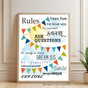 May include: A framed print with a light wood frame. The print features the word "Rules" at the top, with other positive words like "Share", "Dream Big", and "Smile". Colorful bunting and a sun graphic decorate the print.