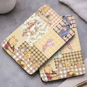May include: Two tablet cases with a patchwork design featuring Winnie the Pooh and friends. The design includes images of Pooh, Tigger, Piglet, and Eeyore on a yellow and brown plaid and floral background.