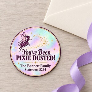 May include: A circular sticker with a pastel watercolor background featuring a dark purple fairy silhouette and gold stars. The text reads: You've Been PIXIE DUSTED! The Bennett Family Stateroom 8264. The sticker has a thin gold border and dark purple edge.