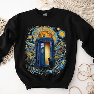 May include: Black sweatshirt with a blue police box design, open door, and a black cat, set against a swirling starry night background. The design is in the style of Van Gogh. The sweatshirt has long sleeves and a crew neck.