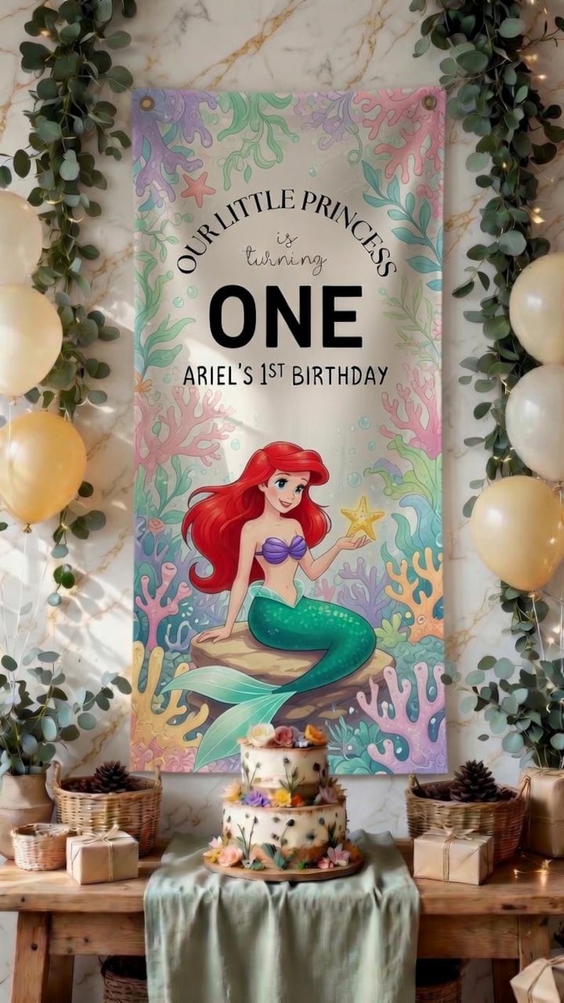 May include: A vertical rectangular banner featuring a cartoon mermaid with red hair and a green tail sitting on a rock, surrounded by colorful coral. The text reads: OUR LITTLE PRINCESS is turning ONE ARIEL'S 1ST BIRTHDAY. The background is light.
