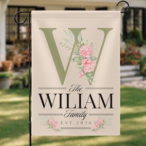 May include: A beige garden flag featuring a large green letter "W" decorated with pink roses and foliage. The flag reads "The WILLIAM Family" and "EST. 2026" in black text, with floral details.