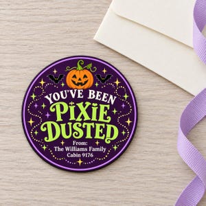 May include: A circular sticker with a dark purple background featuring a central orange jack-o'-lantern, two black bats, and yellow stars. The text reads: YOU'VE BEEN PIXIE DUSTED, From: The Williams Family, Cabin 9176, in white and lime green lettering.