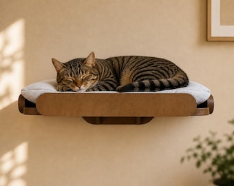 May include: A tabby cat is curled up asleep on a wall-mounted cat bed. The bed has a light gray cushion and a brown wooden frame. The cat's fur is brown with black stripes. The wall is a light beige color.
