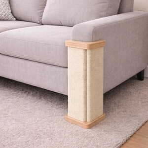 Puede incluir: Un rascador para gatos con una superficie para rascar de sisal beige claro y molduras de madera. El poste es rectangular y est&aacute; colocado junto a un sof&aacute; gris sobre una alfombra gris. El sisal est&aacute; envuelto alrededor de un marco de madera.
