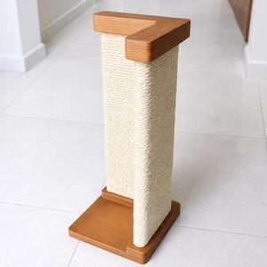 Puede incluir: Un rascador para gatos de madera con una superficie para rascar de cuerda natural. El poste tiene una base cuadrada y una pieza superior, ambas de madera de color marr&oacute;n claro. La cuerda de sisal est&aacute; enrollada alrededor de la columna central. Un dise&ntilde;o moderno de muebles para gatos.