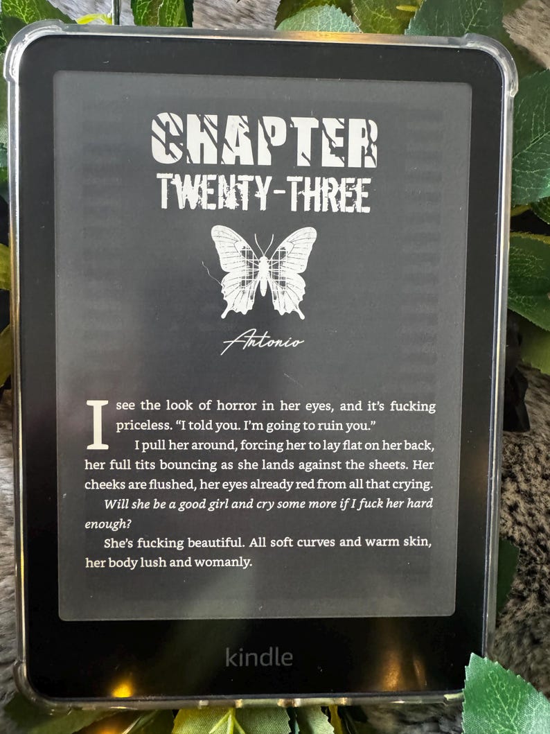 K&ouml;nnte beinhalten: Ein Kindle E-Reader, der eine Buchseite mit dem Titel "Chapter Twenty-Three" und einer Schmetterlingsgrafik anzeigt. Der Text enth&auml;lt den Namen des Autors, "Antonio", und einen Textauszug. Das Ger&auml;t befindet sich in einer transparenten Schutzh&uuml;lle.