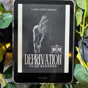 Può includere: Un e-reader Kindle nero che mostra la copertina del libro "Deprivation" di Ellie Sanders. La copertina presenta un'immagine in scala di grigi di una persona legata. Il testo "A Dark Captive Romance" è in alto.