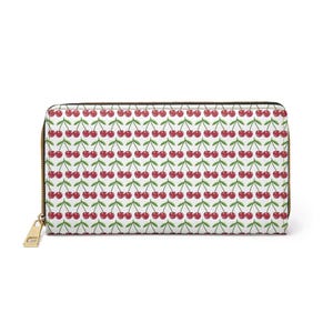 May include: A white wallet with a repeating pattern of red cherries and green stems. The wallet has a gold zipper and a gold zipper pull. The wallet is rectangular in shape.