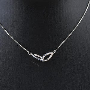 Puede incluir: Un collar plateado con una cadena fina y un colgante con dos formas ovaladas abiertas entrelazadas. El colgante está adornado con pequeñas piedras brillantes, exhibido en un expositor de joyas negro.