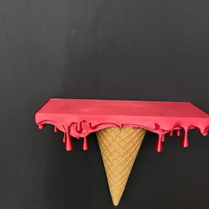 May include: A wall-mounted shelf featuring a flat rectangular top surface in a vibrant red finish with realistic dripping paint effects along the edges, supported by a textured, tan-colored inverted ice cream cone base design.