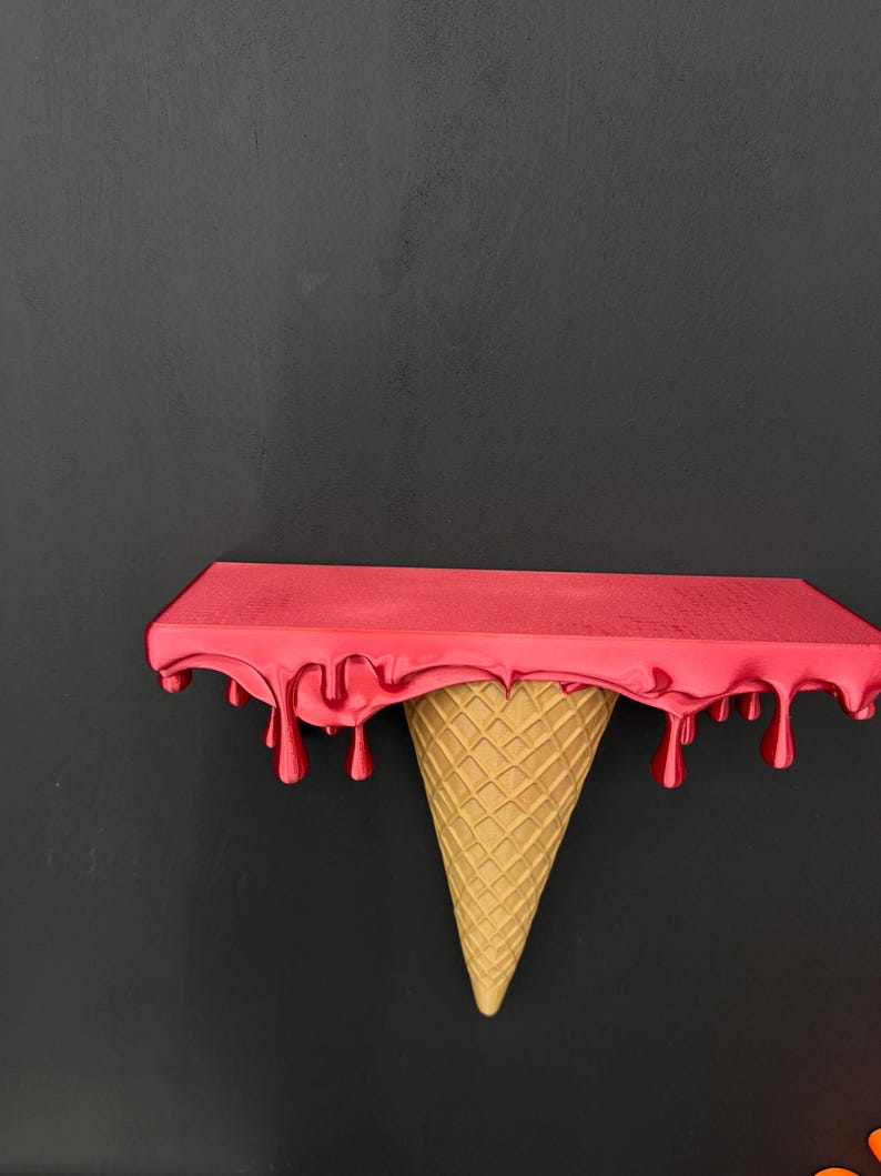 May include: A wall-mounted shelf featuring a flat rectangular top surface in a vibrant red finish with realistic dripping paint effects along the edges, supported by a textured, tan-colored inverted ice cream cone base design.