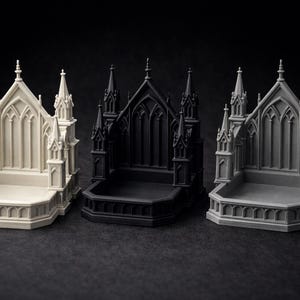 K&ouml;nnte beinhalten: Drei Miniaturmodelle gotischer Kathedralen in Off-White, Schwarz und Grau. Jedes Modell weist aufwendige architektonische Details auf, darunter T&uuml;rme, Spitzbogenfenster und einen rechteckigen Sockel. Die Modelle werden vor einem dunklen Hintergrund pr&auml;sentiert.