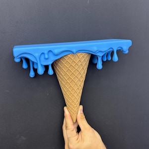 May include: A wall shelf shaped like an upside-down ice cream cone. The top flat surface is bright blue with a dripping liquid effect along the edges. The base is a tan, textured cone with a classic waffle grid pattern on the exterior surface.
