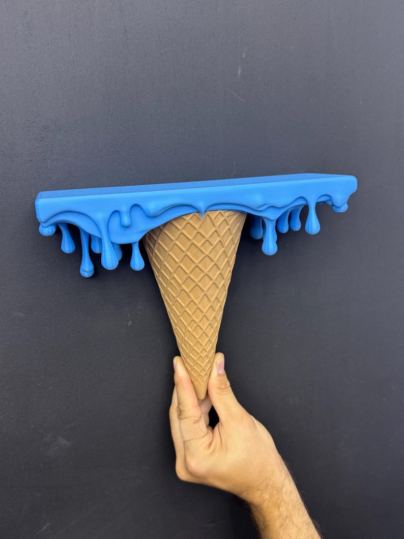 May include: A wall shelf shaped like an upside-down ice cream cone. The top flat surface is bright blue with a dripping liquid effect along the edges. The base is a tan, textured cone with a classic waffle grid pattern on the exterior surface.