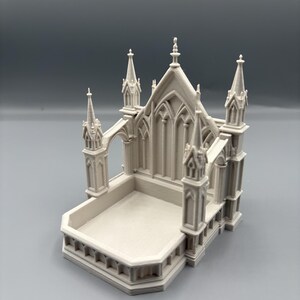 K&ouml;nnte beinhalten: Hellgraues Miniatur-Kathedralenmodell mit aufwendigen architektonischen Details. Das Modell verf&uuml;gt &uuml;ber Spitzb&ouml;gen, T&uuml;rme und eine rechteckige Basis. Das Design erinnert an gotische Architektur.
