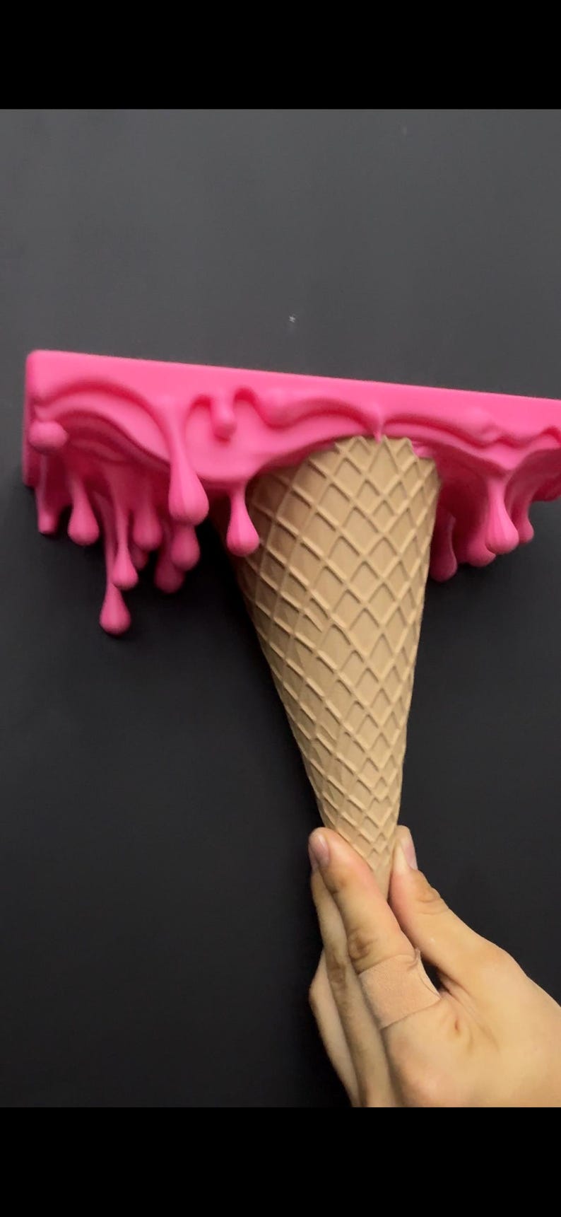 May include: A wall shelf shaped like an upside-down ice cream cone with a tan waffle-textured cone base and a bright pink rectangular top section featuring a realistic dripping liquid effect that hangs down over the edges of the shelf surface.