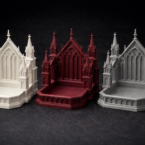 K&ouml;nnte beinhalten: Drei Miniaturmodelle einer gotischen Kathedrale in Wei&szlig;, Burgunderrot und Grau. Jedes Modell weist aufwendige architektonische Details auf, darunter T&uuml;rme, Spitzbogenfenster und einen rechteckigen Sockel. Die Modelle werden auf einer dunklen Oberfl&auml;che pr&auml;sentiert.