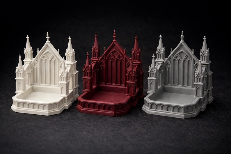 K&ouml;nnte beinhalten: Drei Miniaturmodelle einer gotischen Kathedrale in Wei&szlig;, Burgunderrot und Grau. Jedes Modell weist aufwendige architektonische Details auf, darunter T&uuml;rme, Spitzbogenfenster und einen rechteckigen Sockel. Die Modelle werden auf einer dunklen Oberfl&auml;che pr&auml;sentiert.