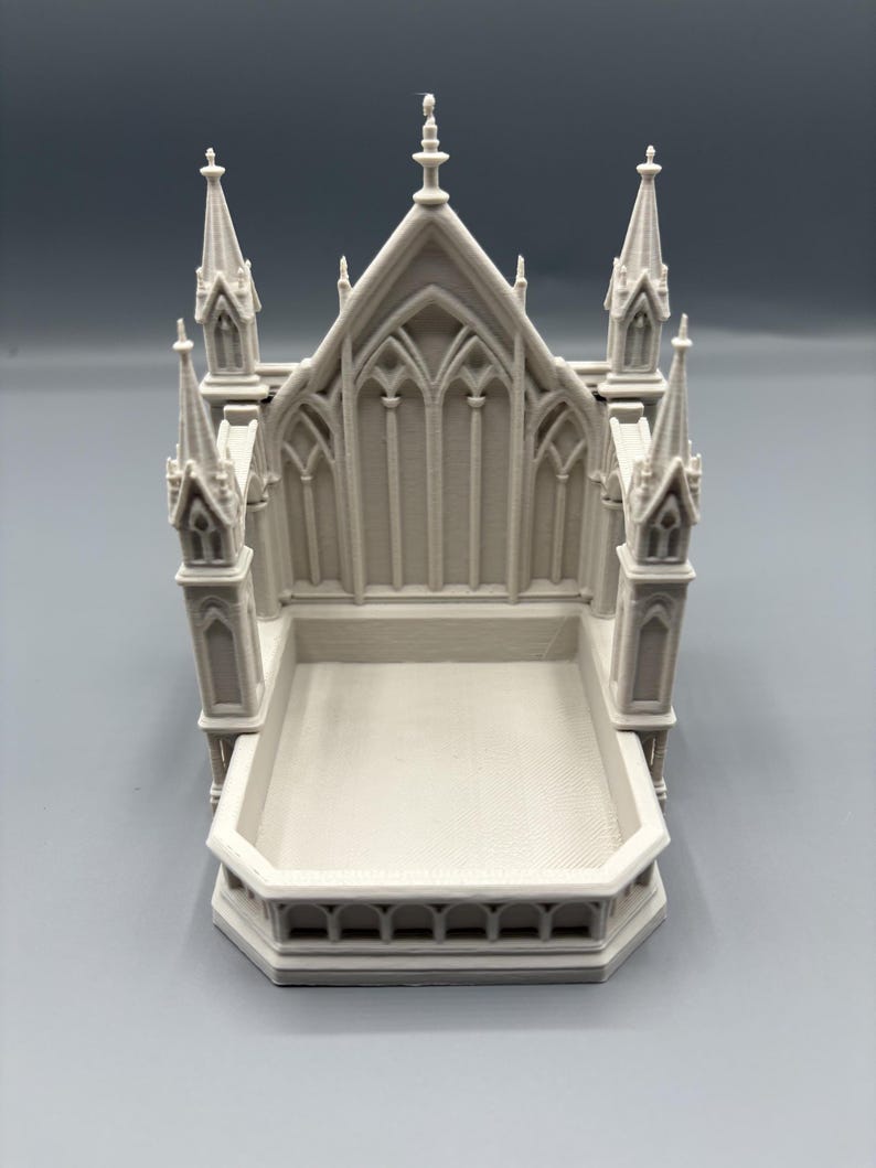 K&ouml;nnte beinhalten: Ein 3D-gedrucktes, cremefarbenes Miniatur-Kathedralenmodell. Das Modell weist detaillierte architektonische Elemente auf, darunter T&uuml;rme, Bogenfenster und eine rechteckige Basis. Das Design erinnert an gotische Architektur.