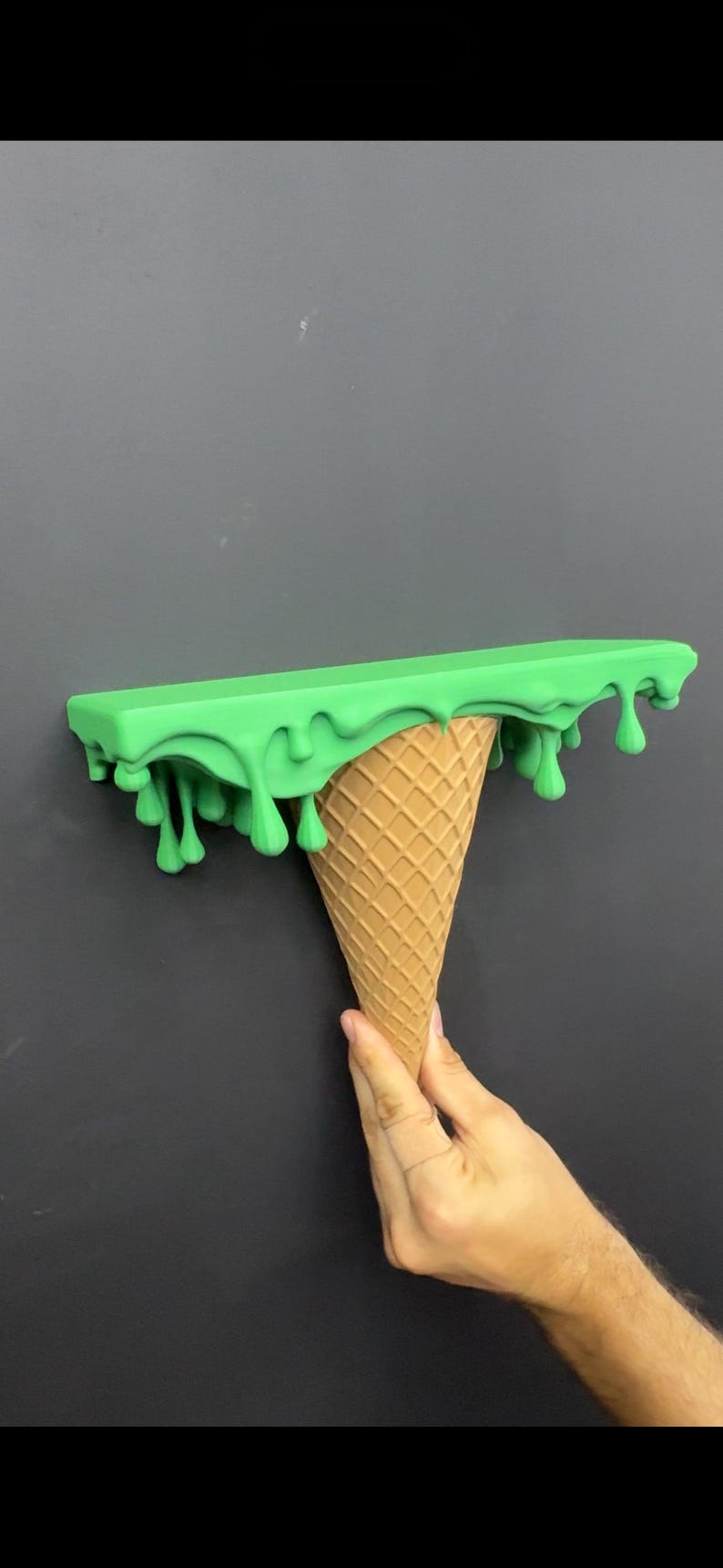 May include: A wall-mounted shelf featuring a flat, rectangular top surface in bright green with a realistic dripping effect along the edges, supported by a textured, tan-colored cone base that resembles a classic waffle ice cream cone.