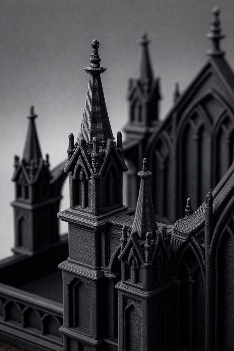K&ouml;nnte beinhalten: Ein detailliertes, graustufiges 3D-gedrucktes Modell einer gotischen Kathedrale. Das Modell weist komplizierte architektonische Details auf, darunter T&uuml;rme, Bogenfenster und dekorative Elemente. Die dunkelgraue Farbe und die strukturierte Oberfl&auml;che verleihen ihm ein realistisches Aussehen.