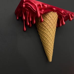 May include: A wall-mounted shelf shaped like an upside-down ice cream cone. The top section features a glossy, metallic red finish with realistic drips cascading down the sides, while the bottom is a textured, tan-colored waffle cone.