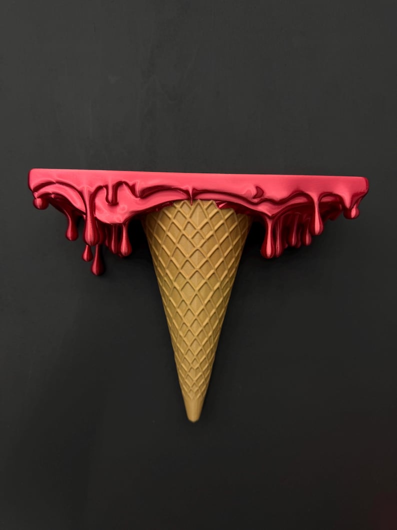 May include: A wall-mounted shelf shaped like an ice cream cone. The top flat surface features a glossy, metallic red finish with realistic drips cascading down the sides, while the base is a textured, tan-colored waffle cone shape.