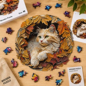 Op de afbeelding: Een ronde houten puzzel met een pluizige rosse kat genesteld tussen kleurrijke herfstbladeren. De puzzel bevat uniek gevormde stukjes, een referentiekaart en een doos met het label Size: M. De kat heeft groene ogen.