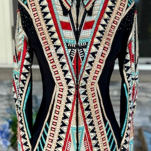 May include: Black show jacket with intricate geometric patterns in red, turquoise, and gold. The jacket is embellished with sparkling rhinestones and features a tailored fit. A stylish equestrian apparel item.