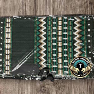 Peut inclure: Un nouveau tapis de selle pour cheval dans un emballage plastique transparent. Le tapis présente une base vert foncé avec un motif géométrique blanc, beige et vert. Le tapis a une pièce de cuir noir attachée.