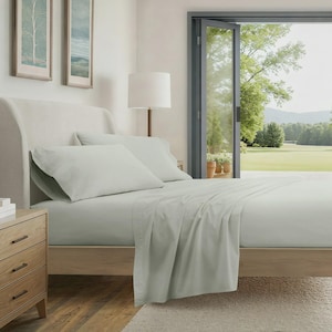 May include: A bed with light green sheets and pillowcases. The bed has a light-colored wooden frame and headboard. A wooden nightstand with three drawers is on the left. The room has a large window with a view of a green landscape.
