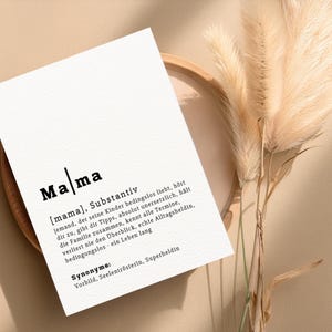 May include: A white card with the German word "Mama" in bold black letters. The card includes a definition and synonyms in German. The card is placed on a wooden tray with dried ornamental grass.