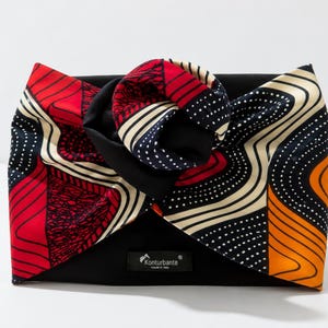 Può includere: Una pochette nera con un fiocco colorato. Il fiocco presenta disegni rossi, bianchi, blu navy e arancioni. La pochette ha una piccola etichetta con la scritta "Konturbante" e "made in Italy".