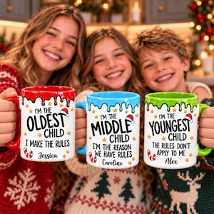 May include: Three white ceramic mugs with colorful drip-style rims in red, blue, and green. Each mug features Christmas-themed text: I'm the oldest child, I'm the middle child, and I'm the youngest child, personalized with names Jessica, Caroline, and Alex.