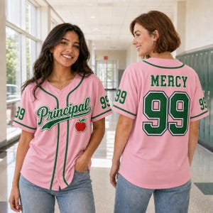 May include: A light pink baseball jersey with dark green trim, featuring the word Principal in script, a red apple graphic, and the number 99 on the front. The back displays the name MERCY and the number 99 in dark green with white outlines.